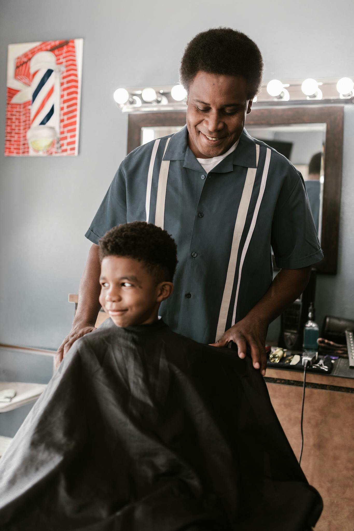 A barber prepares to cut a boy's hair in a barbershop, both smiling and enjoying the moment.